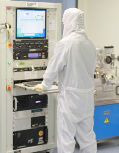 A person wearing a cleanroom suit works on a computer in a lab.