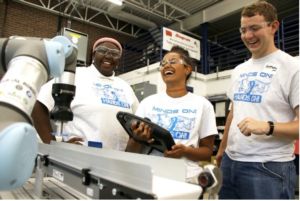 Several students laugh together while controlling a robot arm 