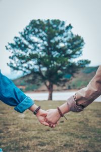This image shows two hands clasped in front of a tree. One wears a watch and the other a bracelet. 