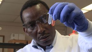 A photo of Gerald Kinyua in a lab coat, holding a test tube
