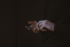 A photo of hands holding a phone in front of a dark background